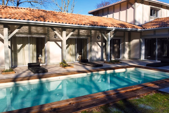 Maison landaise à étage avec piscine rectangulaire, grande terrasse en bois et larges baies vitrées.