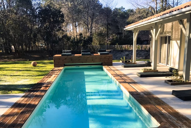 Piscine rectangulaire bordée d'une plage en bois avec transats, sur la terrasse d'une maison.