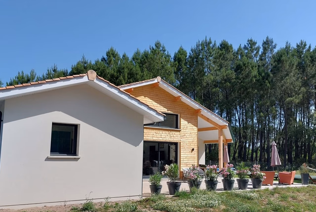 Façade de maison de plain-pied avec bardage bois, enduit clair, grande baie vitrée et terrasse.