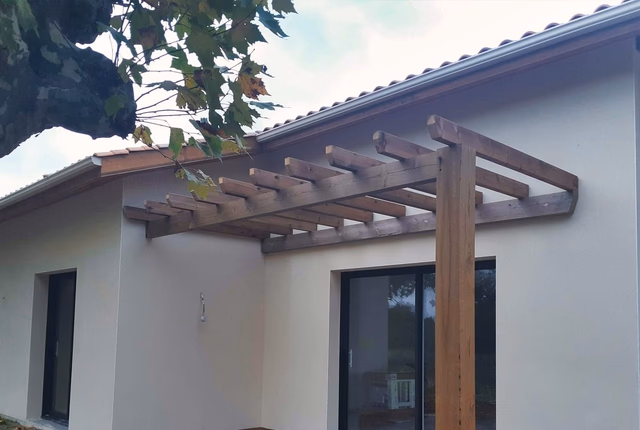 Façade claire d'une villa de plain-pied avec pergola en bois adossée au-dessus d'une baie vitrée.