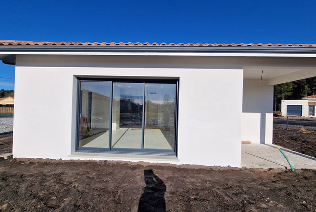 Façade blanche d'une maison de plain-pied à Téthieu avec grande baie vitrée et porche d'entrée.