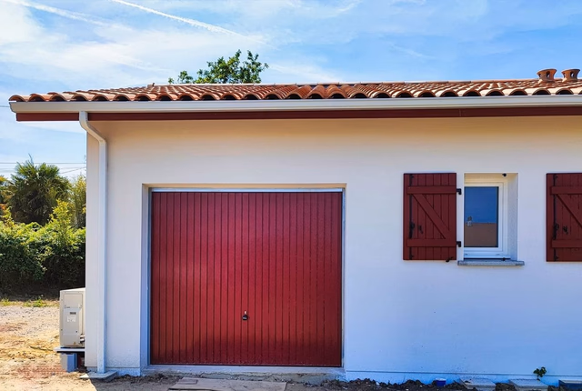 Façade de maison de plain-pied avec toiture en tuiles, porte de garage et volets battants rouges.