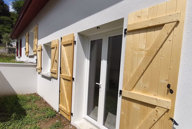 Façade blanche d'une maison avec des volets en bois clair et une porte-fenêtre vitrée.