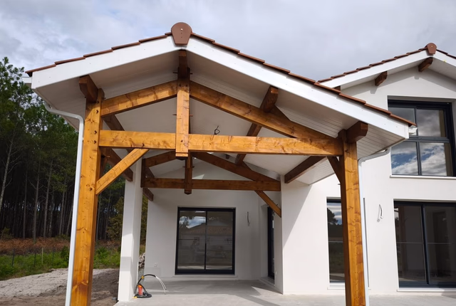 Façade blanche d'une maison avec charpente en bois apparente abritant une terrasse sous auvent.