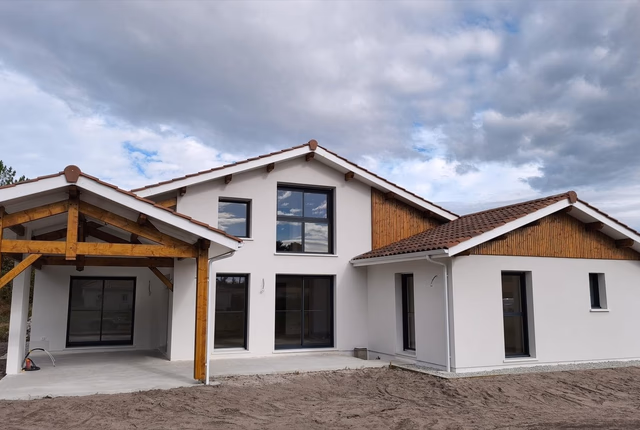 Façade de maison contemporaine en enduit blanc avec toiture en tuiles et auvent en bois.