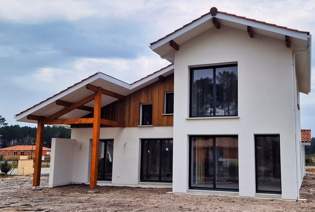 Façade extérieure d'une villa R+1 moderne avec enduit blanc, bardage bois et grande toiture en tuiles.