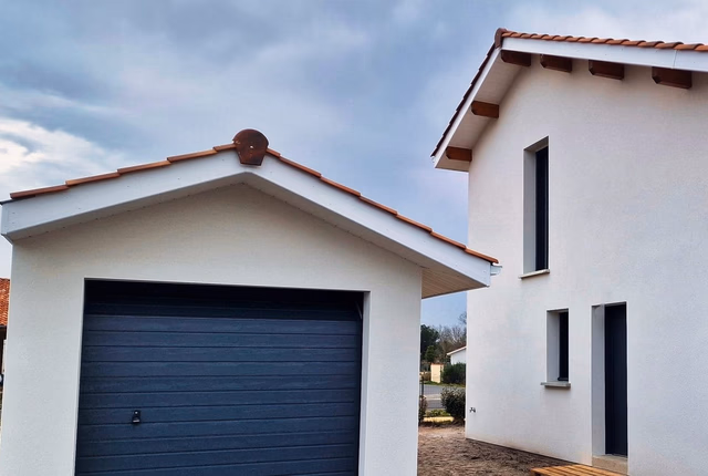 Maison individuelle à étage aux murs blancs avec toiture en tuiles et garage attenant.