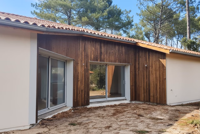 Façade de maison en bois et crémeux avec deux grandes baies vitrées coulissantes en aluminium.