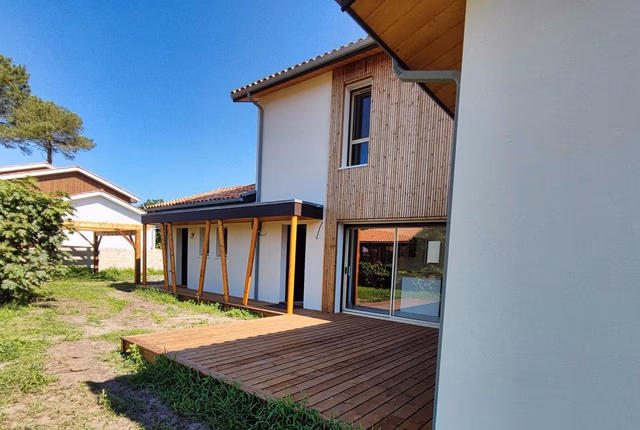 Façade arrière d'une villa contemporaine avec bardage bois, enduit clair et grande terrasse en bois.