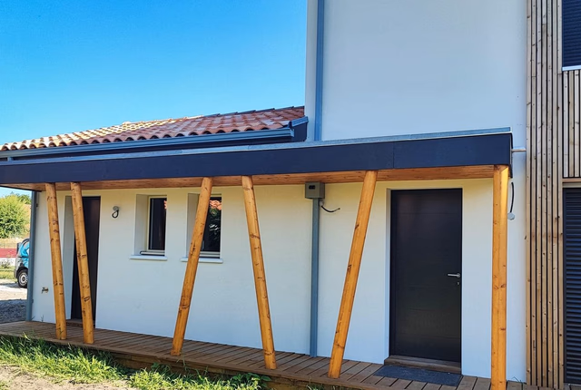 Façade de villa contemporaine avec un auvent en bois soutenu par des poteaux inclinés.