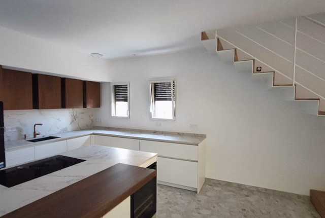 Cuisine moderne blanche ouverte sous un escalier en bois et métal, avec un îlot central et des placards en bois.