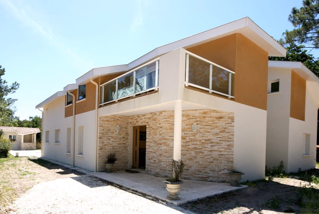 Façade avant d'une grande maison contemporaine à étage avec parement en pierre et balcon vitré.