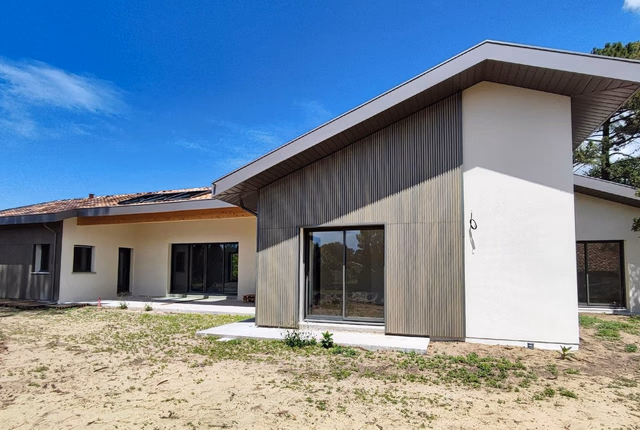 Façade de la villa moderne en enduit blanc et bardage bois rainuré avec larges baies vitrées.