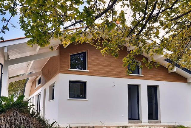 Façade de maison avec enduit blanc, bardage bois à l'étage, fenêtres noires et avancée de toit.