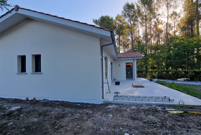 Profil latéral de la maison individuelle avec terrasse extérieure et forêt de pins en arrière-plan à Herm