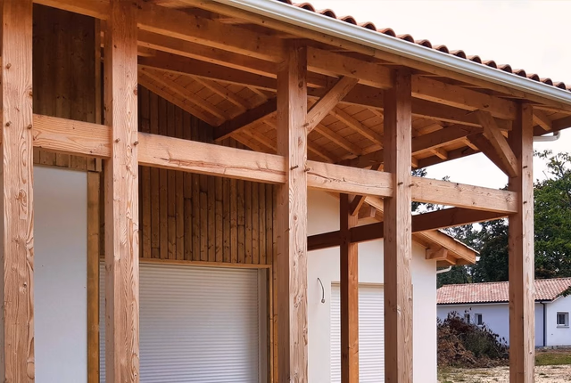 Structure en bois apparente d'un auvent et d'une charpente extérieure soutenant un toit en tuiles.