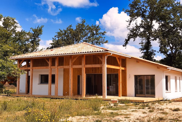 Façade de maison landaise contemporaine avec charpente bois apparente et terrasse en bois.