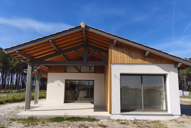 Façade de maison de plain-pied avec bardage bois, larges baies vitrées et terrasse sous auvent.