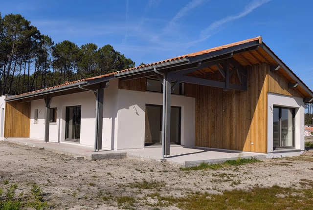Façade extérieure d'une maison de plain-pied avec enduit blanc, bardage bois et terrasse couverte.