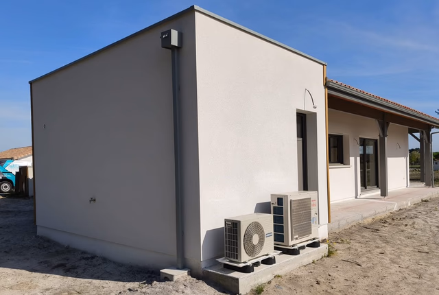 Façade claire d'une maison de plain-pied avec deux unités extérieures de pompe à chaleur au sol.