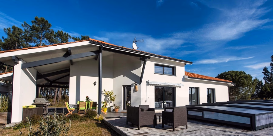 Façade blanche d'une maison contemporaine avec terrasse en bois, mobilier de jardin et abri couvert.