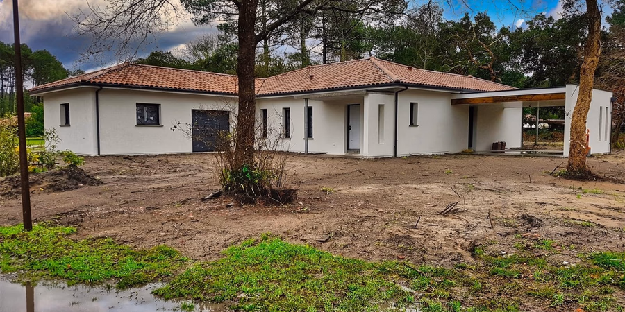Maison de plain-pied blanche à toiture en tuiles avec grand carport et terrain en cours d'aménagement.