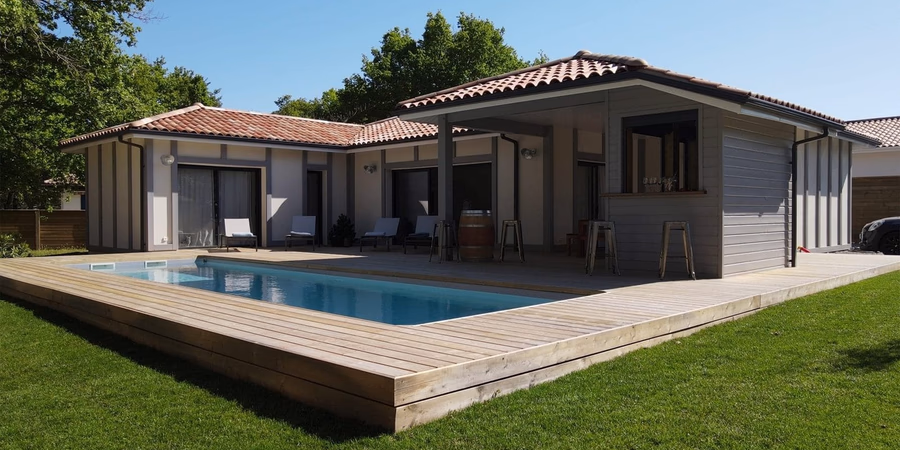 Maison de plain-pied moderne avec piscine rectangulaire encastrée dans une vaste terrasse en bois.