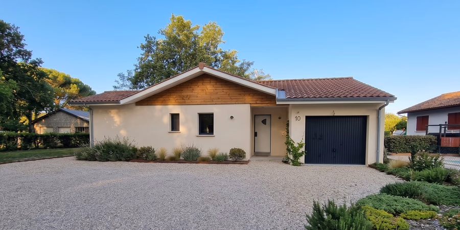 Façade avant de la maison de plain-pied à Herm avec bardage bois sous pignon, cour gravillonnée et garage anthracite