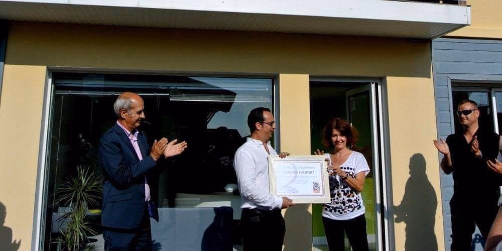 Quatre personnes souriantes applaudissent pendant la remise d'un grand diplôme encadré.