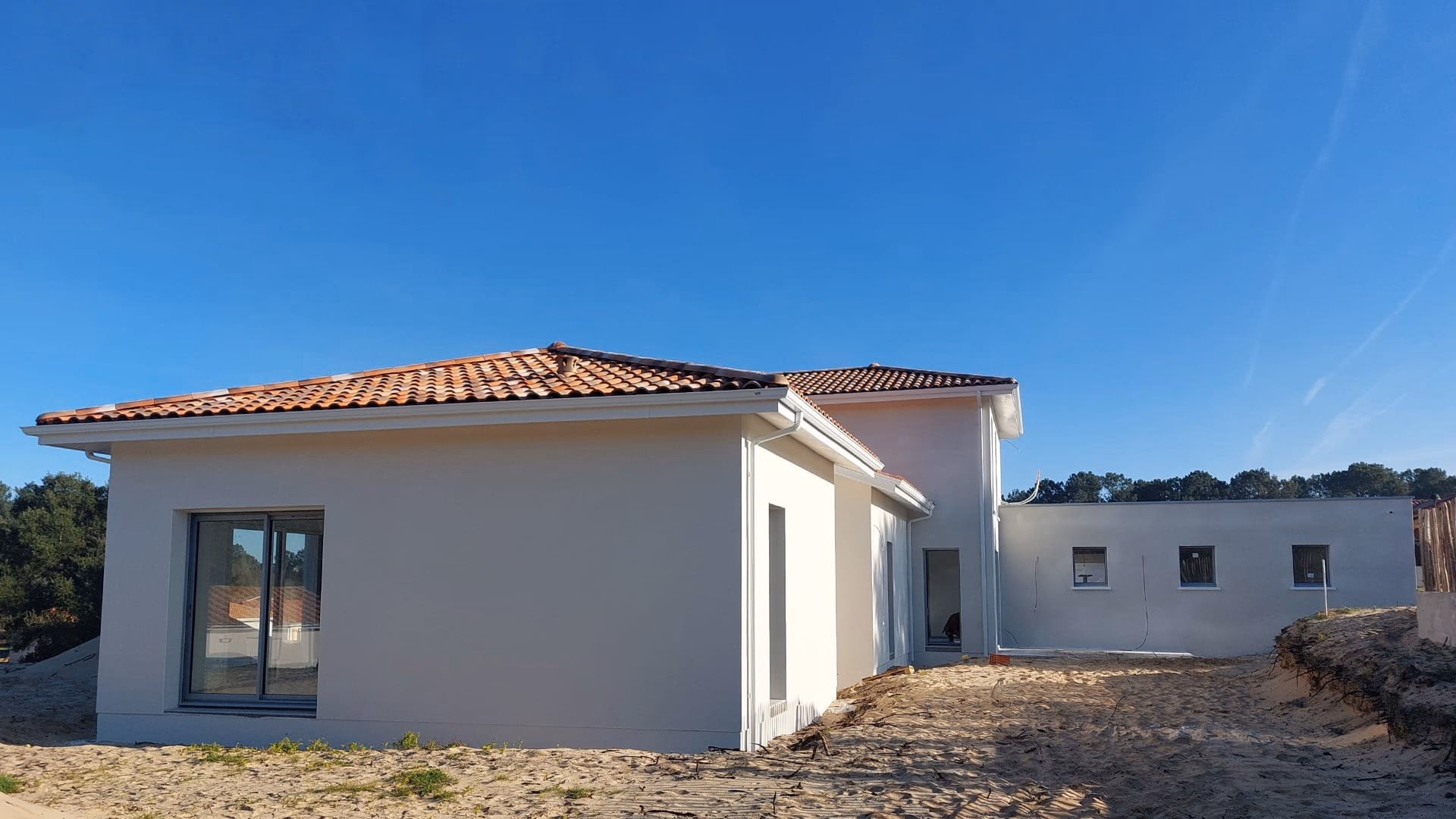 Vue de la façade avant de la nouvelle maison en construction à Lit-et-Mixe, avec son enduit blanc, son toit plat et son étage en tuiles.