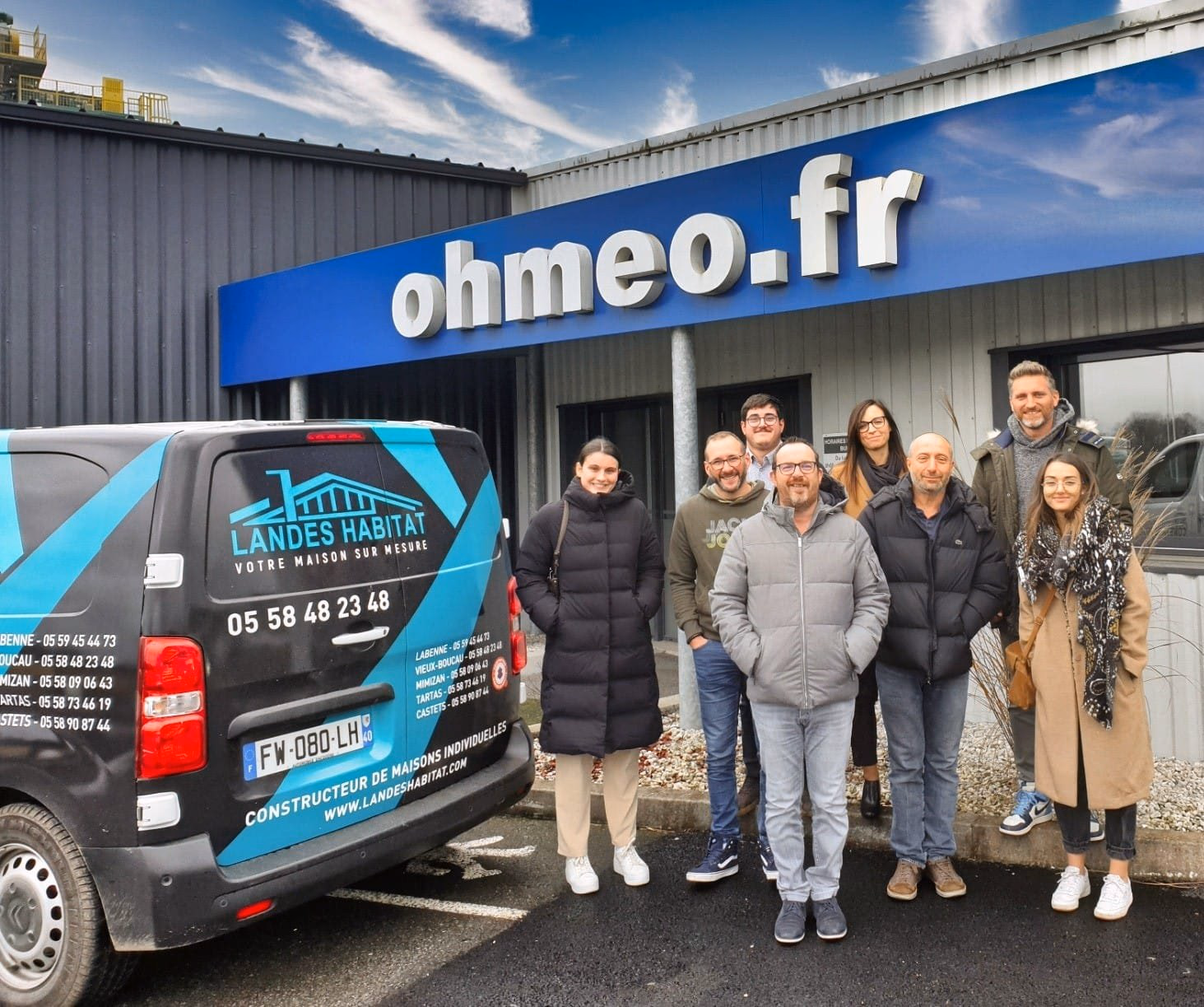 Huit collaborateurs posent souriants devant un bâtiment portant l'enseigne ohmeo.fr à côté d'une fourgonnette Landes Habitat.