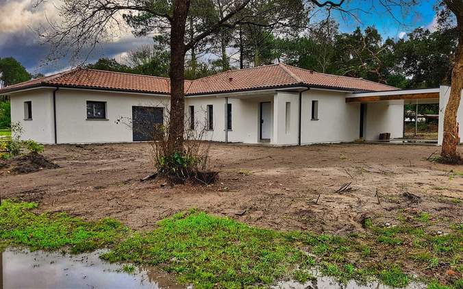 Maison de plain-pied blanche à toiture en tuiles avec grand carport et terrain en cours d'aménagement.