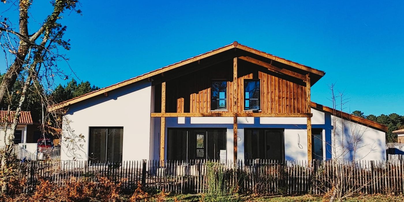 Façade de la maison landaise contemporaine construite à Moliets-et-Maa, alliant bardage bois et crépi blanc.