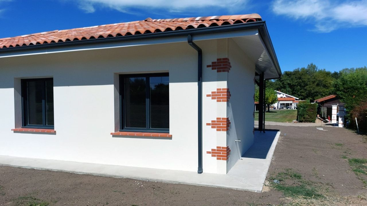 Maison moderne avec façade blanche, fenêtres sombres et toit en tuiles rouges.