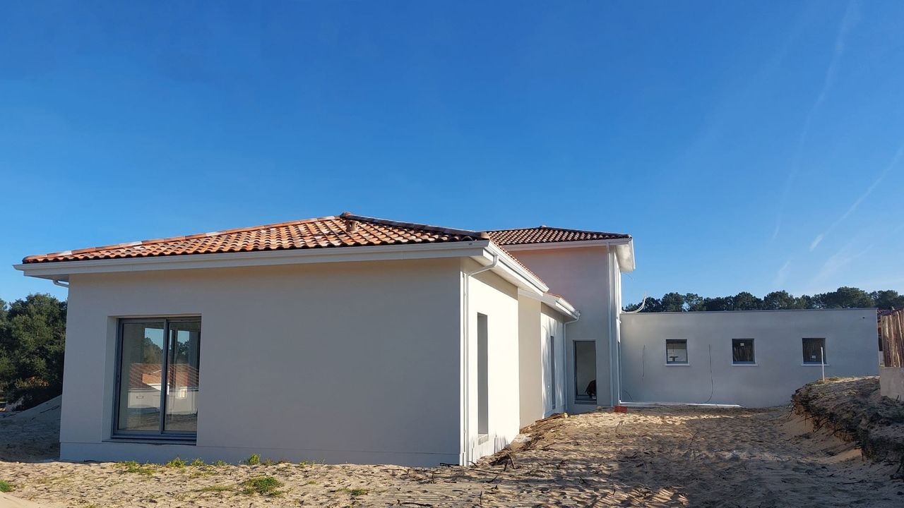 Vue de la façade avant de la nouvelle maison en construction à Lit-et-Mixe, avec son enduit blanc, son toit plat et son étage en tuiles.