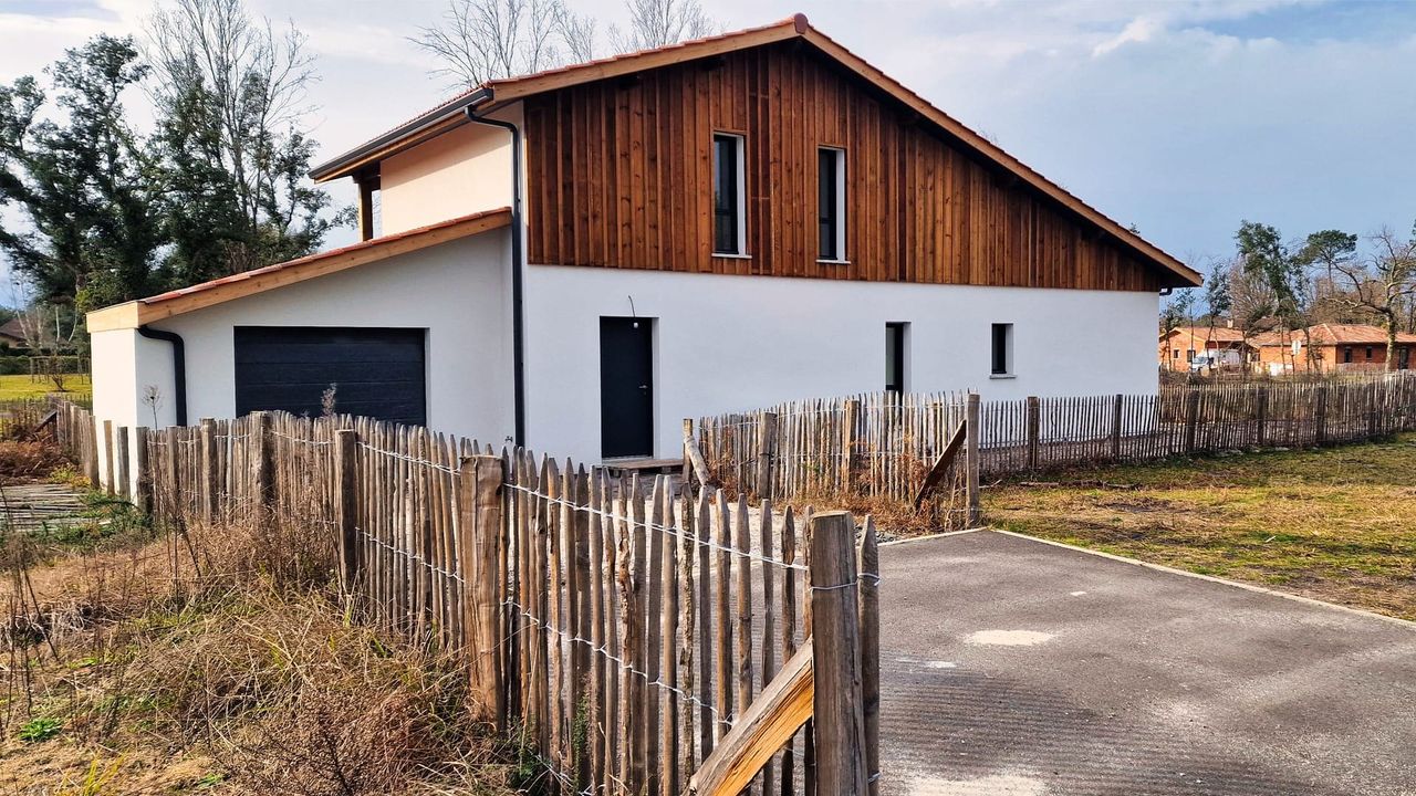Maison moderne à deux étages avec une façade en bois et un garage, entourée d'une clôture en bois.