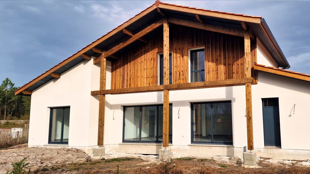 Maison moderne à deux étages avec une façade en bois et des murs blancs, fenêtres en verre.