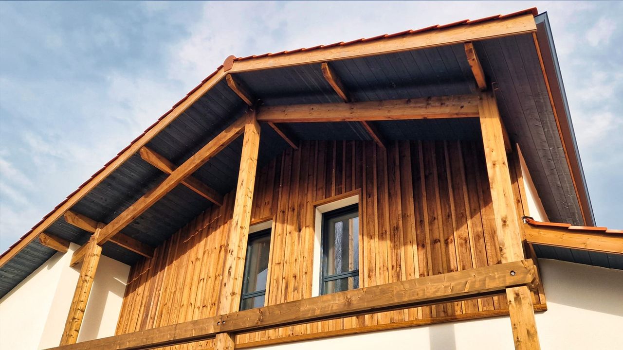 Façade d'une maison en bois avec des poutres apparentes et un toit en pente sous un ciel nuageux.