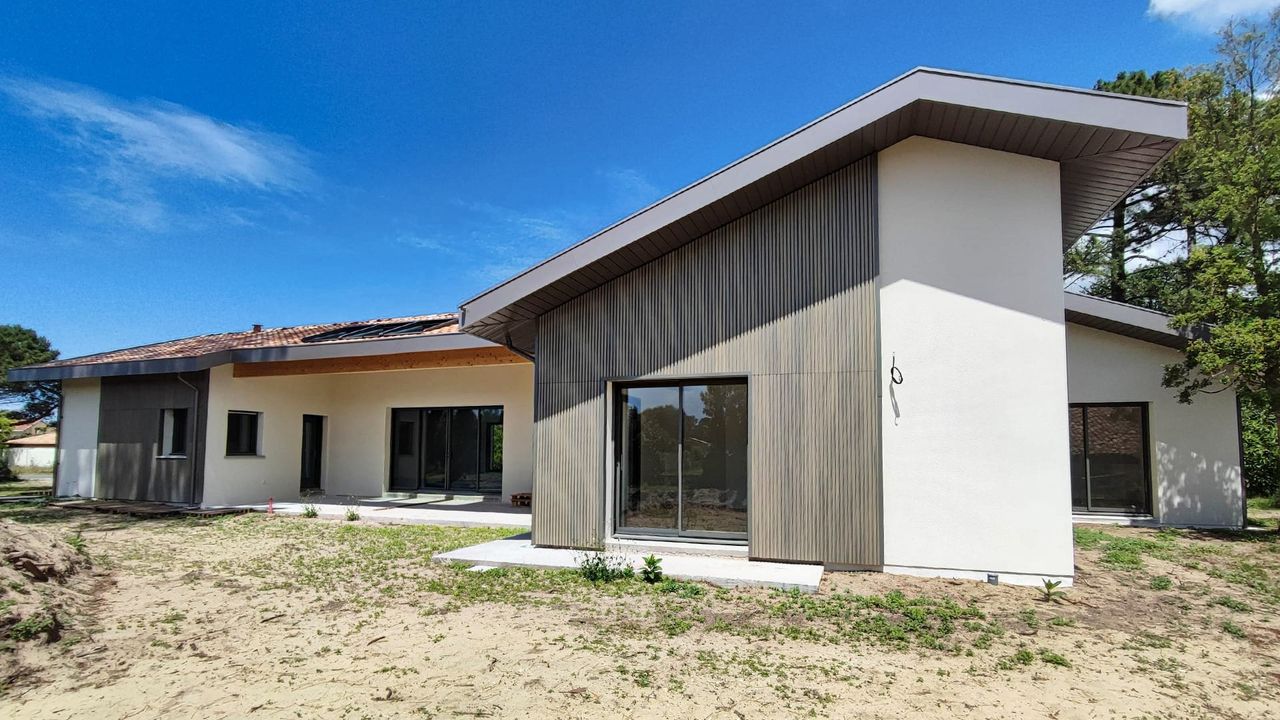 Maison moderne avec un design en bois et des grandes fenêtres, située dans un environnement dégagé.