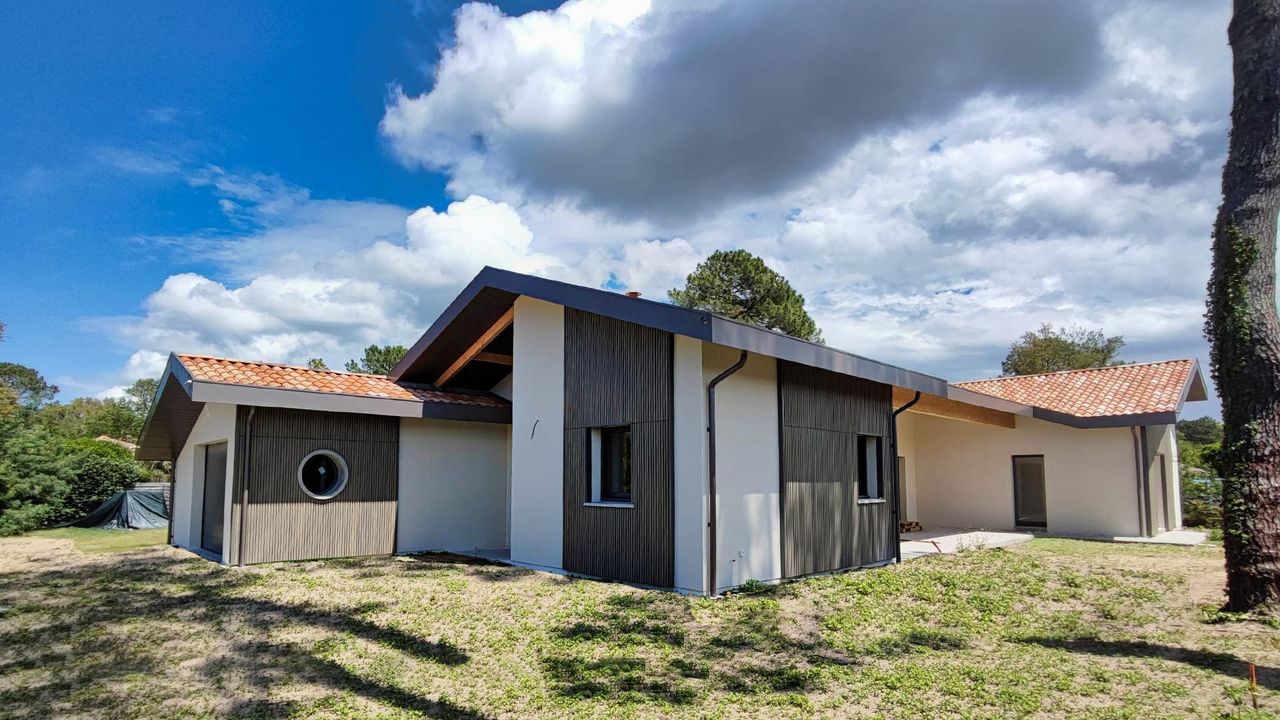 Maison moderne avec un toit en pente et des éléments en bois sur la façade, entourée de verdure.