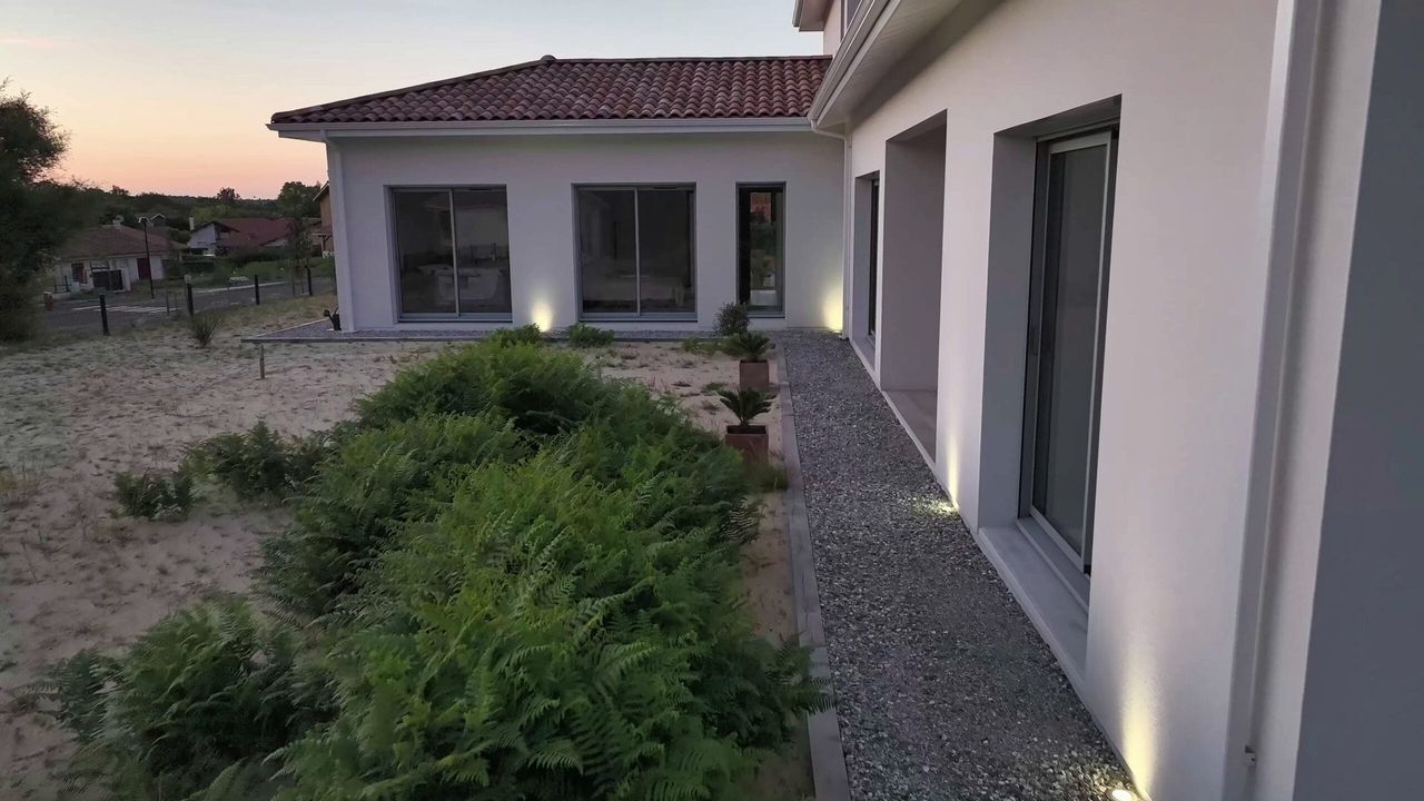 Patio végétalisé avec éclairage LED, grandes baies vitrées et façade blanche à Lit-et-Mixe