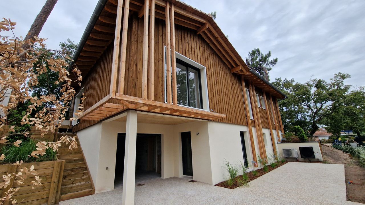 Vue en angle de l'arrière d'une maison contemporaine en bois sur pilotis avec son porche couvert et un escalier d'accès en bois.