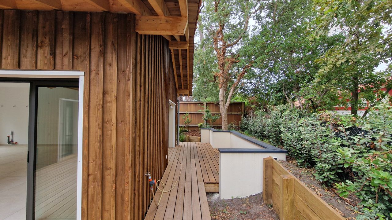 Détail de la terrasse en bois surélevée d'une maison contemporaine, avec un muret de retenue de terre en platelage bois.