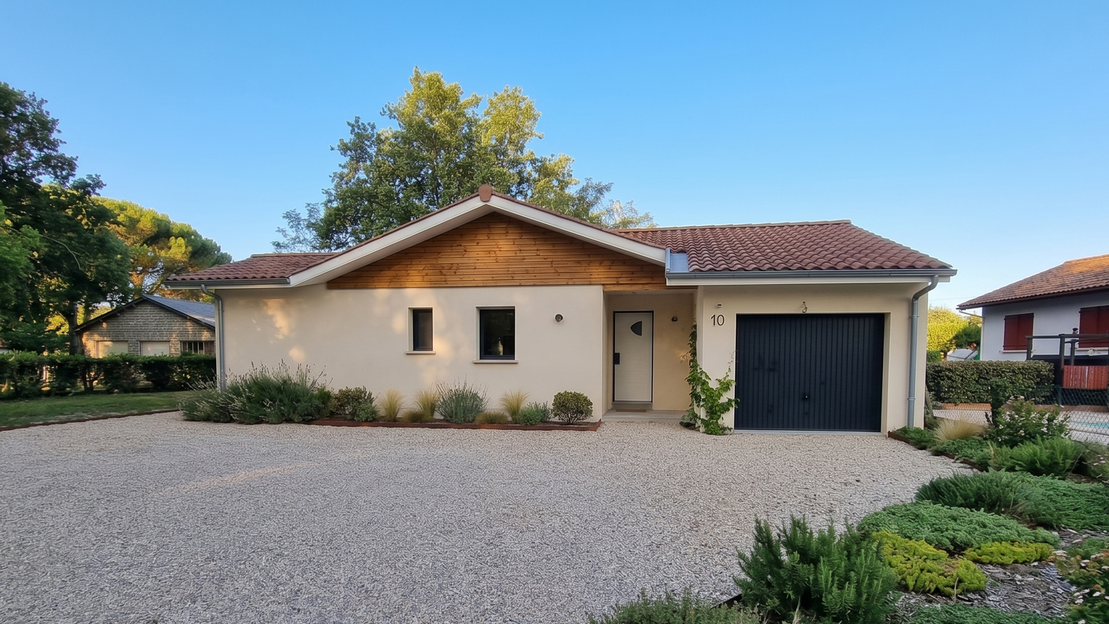 Façade avant de la maison de plain-pied à Herm avec bardage bois sous pignon, cour gravillonnée et garage anthracite