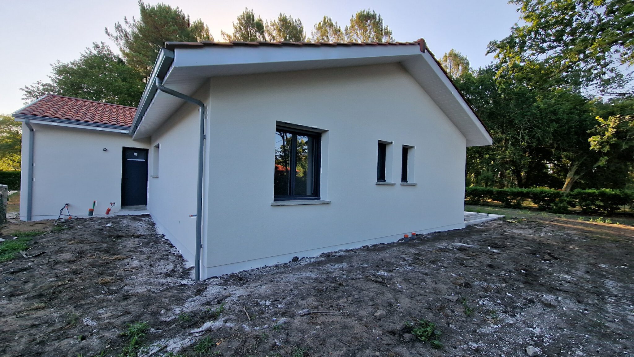 Façade latérale avec fenêtres gris anthracite, débord de toit blanc et terrain arboré à Herm