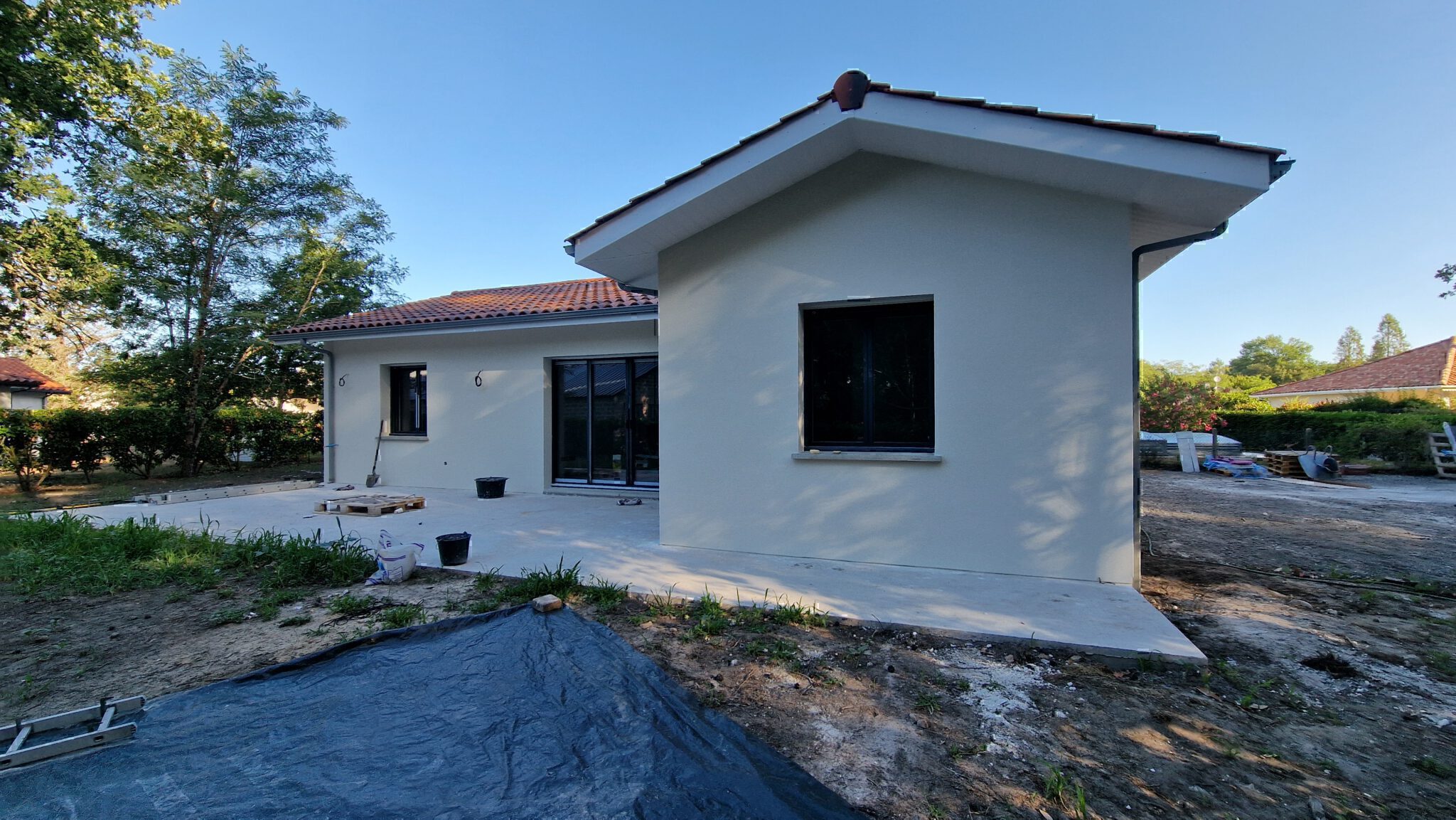 Façade arrière en angle avec dalle terrasse et grande baie vitrée aluminium ouvrant sur le jardin à Herm