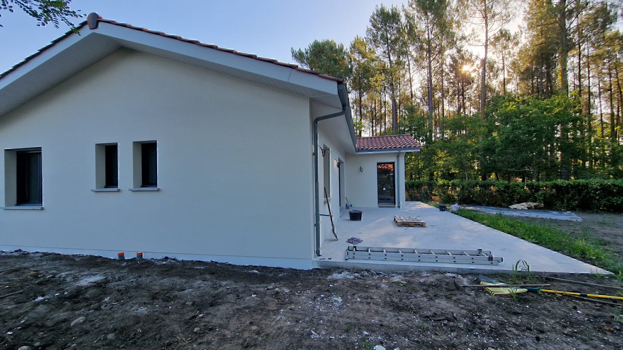 Profil latéral de la maison individuelle avec terrasse extérieure et forêt de pins en arrière-plan à Herm